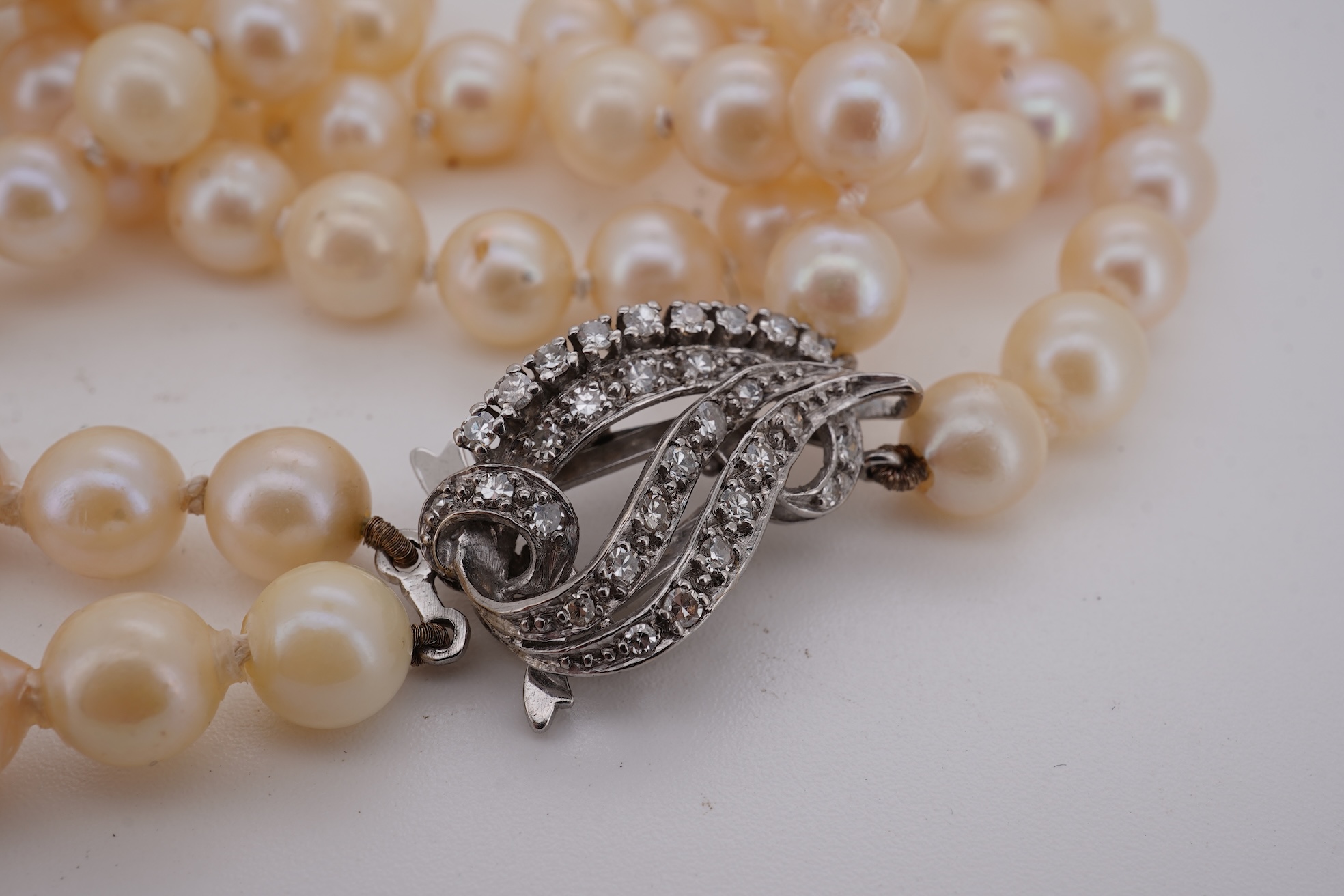 A twin strand cultured pearl necklace with a diamond cluster set white metal scroll shaped clasp, 60cm.
